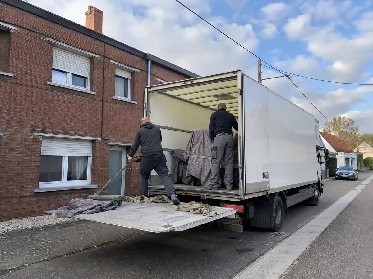 Twee verhuizers zetten meubels in grijze verhuisdekens vast in een verhuiswagen met laadklep