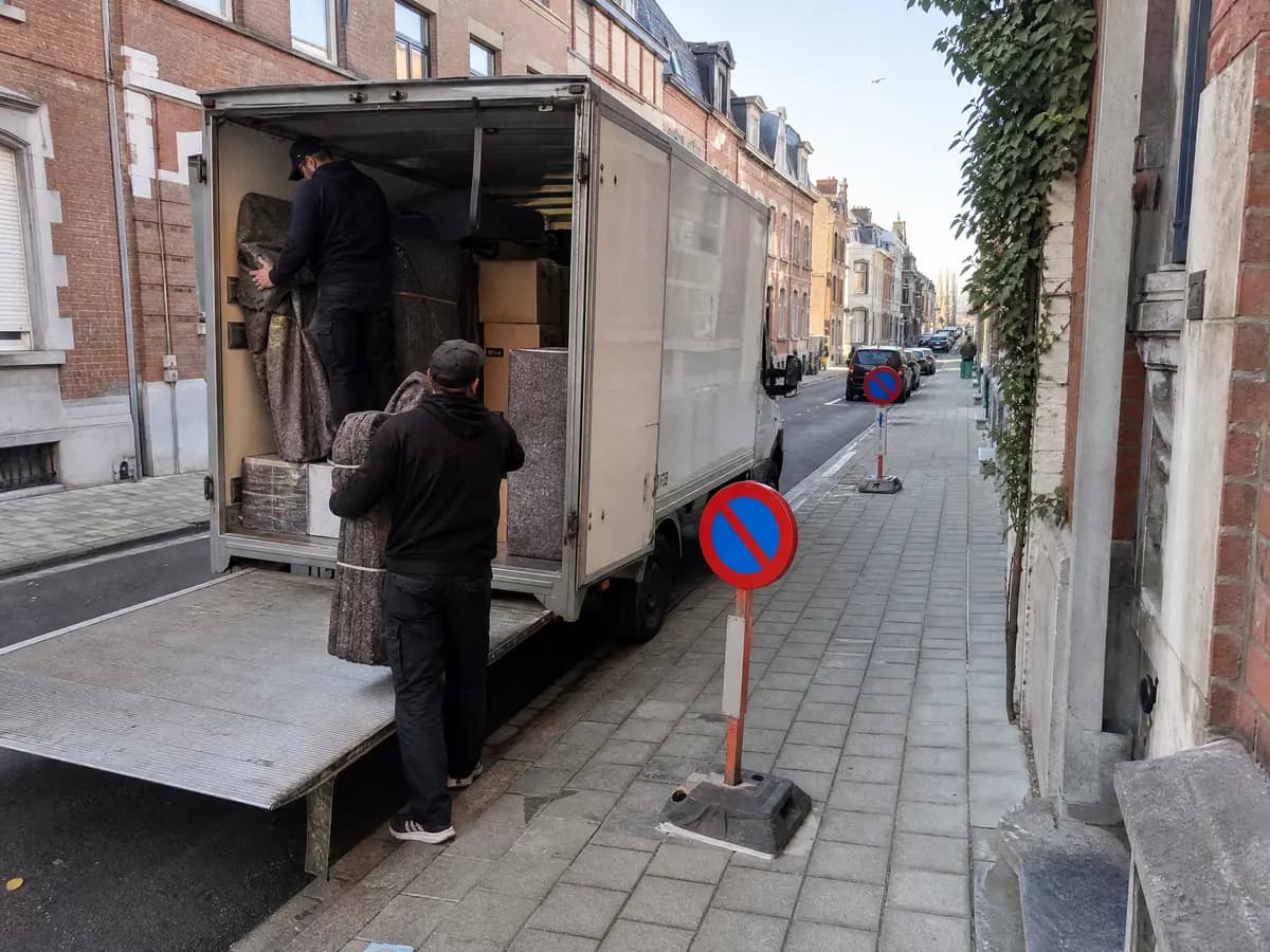 Verhuizers laden vroeg in de ochtend meubels en dozen in een verhuiswagen in een Antwerpse straat met parkeerverbodsborden