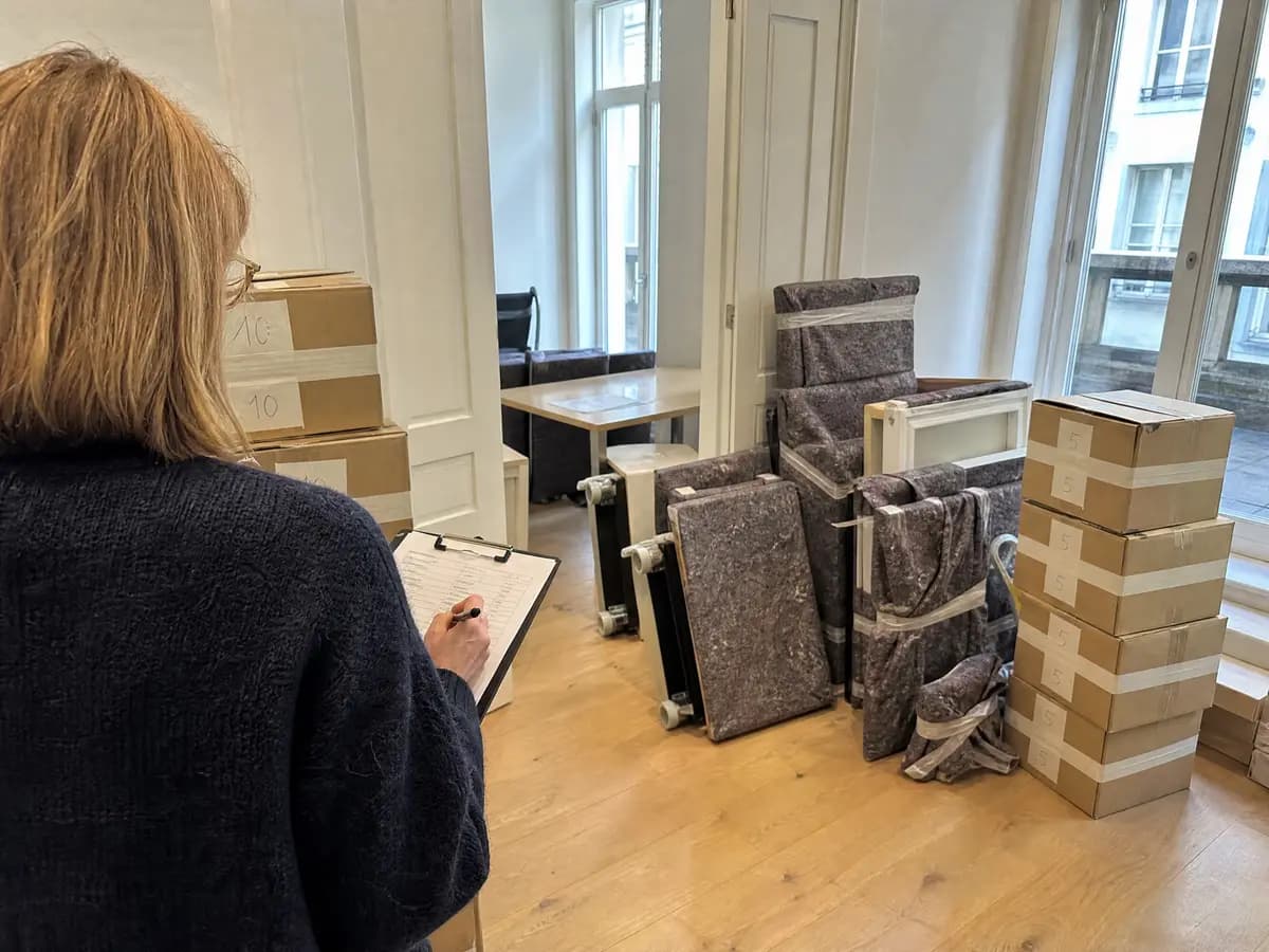 Vrouw met een klembord noteert de inboedel in een woning met ingepakte meubels en gestapelde verhuisdozen
