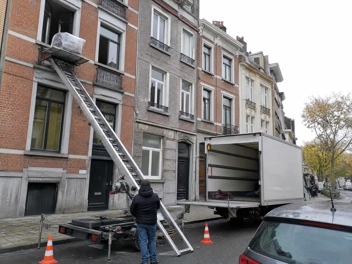 Ladderlift tegen de gevel van een Antwerps herenhuis brengt een ingepakte zetel naar een raam tijdens een verhuis