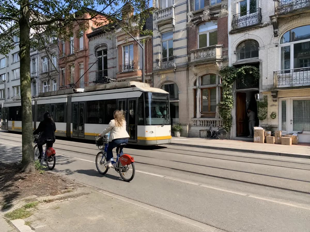 Tram and cyclists in an Antwerp street with moving boxes by a front door, everyday living in Antwerp