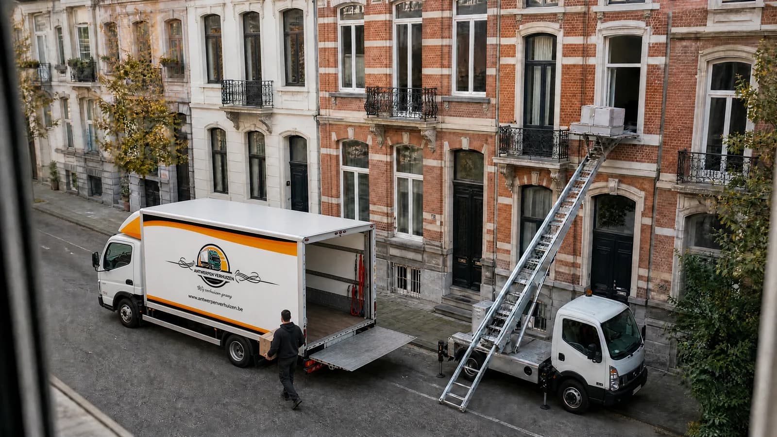 Verhuiswagen van 24 m³ van Antwerpen Verhuizen met open laadruimte en neergelaten laadklep en een ladderlift met dozen aan het raam van de tweede verdieping, in een Antwerpse straat met herenhuizen; een verhuizer draagt een doos naar de wagen