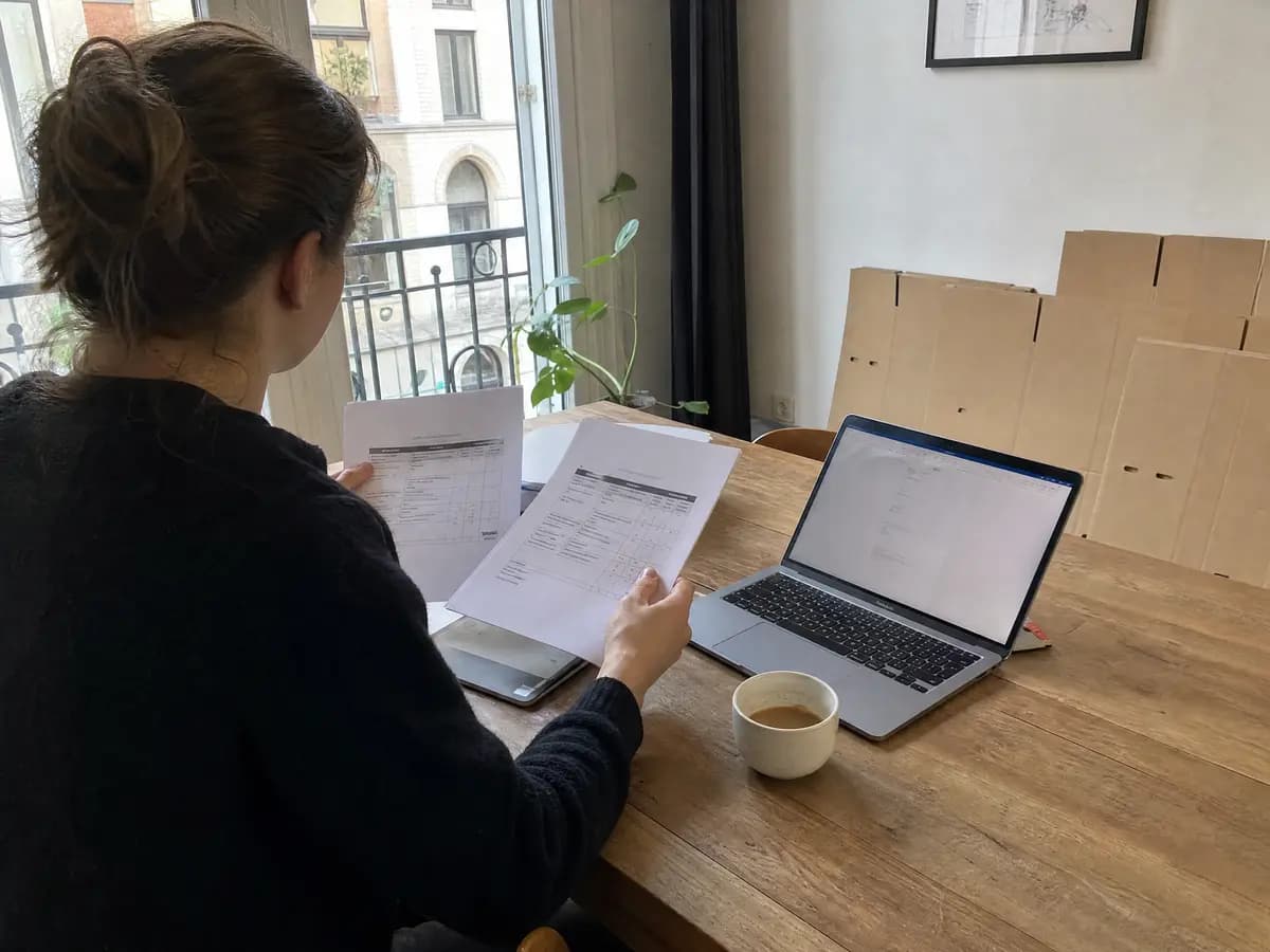 Iemand vergelijkt twee offertes aan de keukentafel om een betrouwbare verhuisfirma in Antwerpen te kiezen