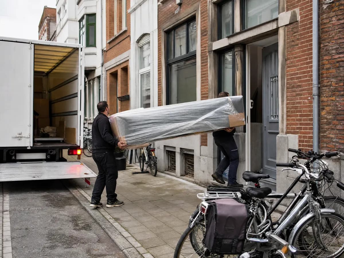 Verhuizers laden meubels uit voor een Nederlandse rijwoning na een verhuis vanuit Antwerpen