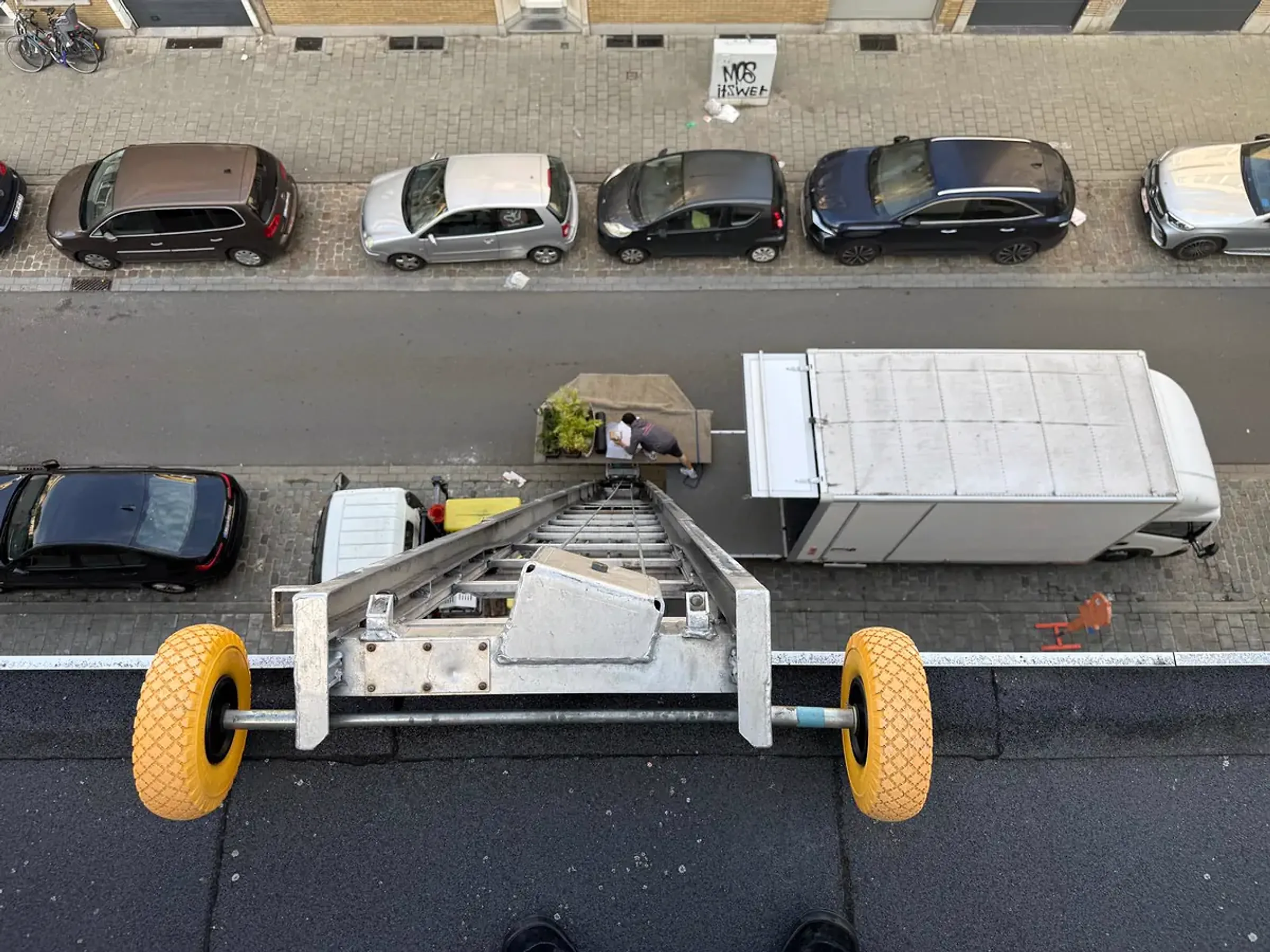 Verhuizen met ladderlift in Deurne: zicht van bovenaan de ladderlift op de straat, met de verhuiswagen en een verhuizer die meubels en planten op het liftplatform zet