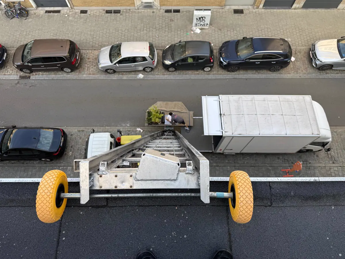 Verhuizen met ladderlift in Deurne: zicht van bovenaan de ladderlift op de straat, met de verhuiswagen en een verhuizer die meubels en planten op het liftplatform zet